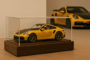 Schaalmodel van een Porsche 911 3.8 Turbo S op vitrine-sokkel, met de echte auto vervaagd op de achtergrond.